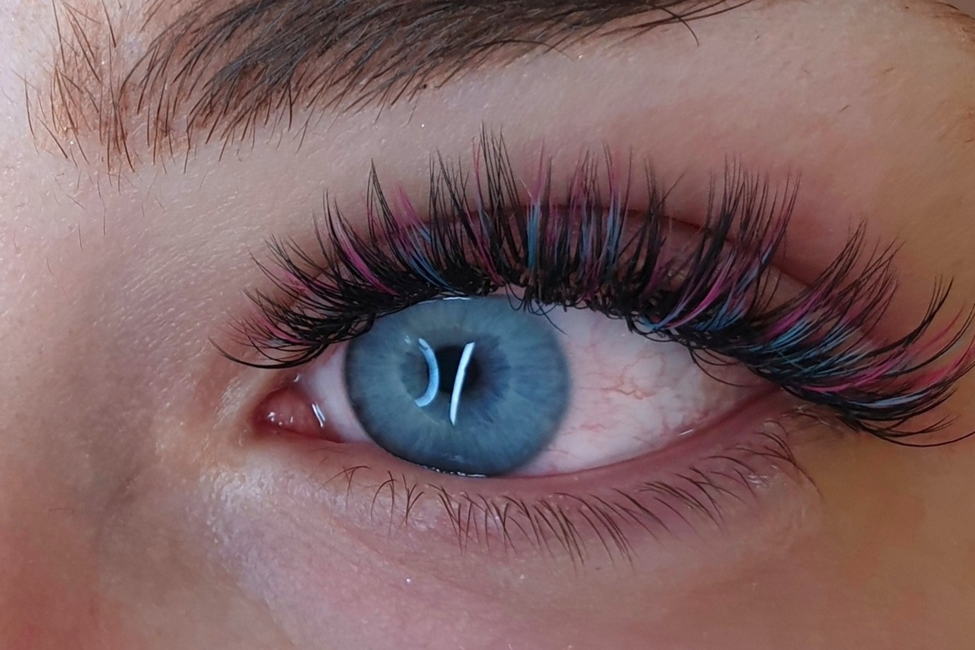 Close-up van een blauw oog met een wimperset in zwart, roze en blauw